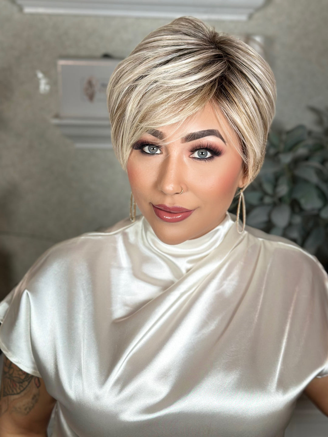 Woman with styled hair wearing a white satin top indoors.
