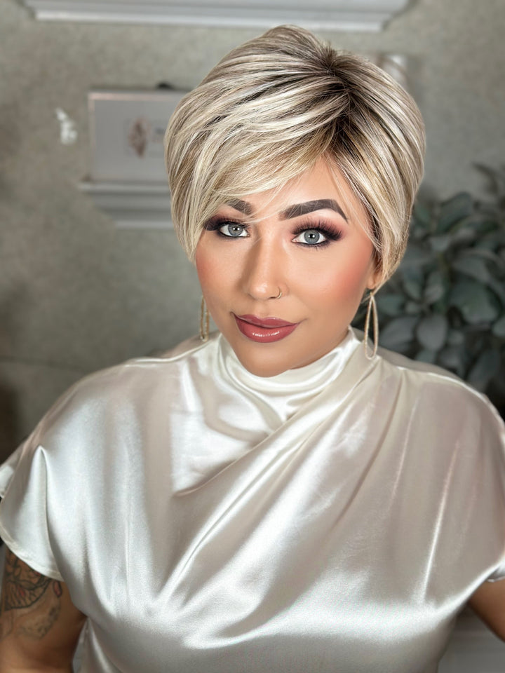 Woman with styled hair wearing a white satin top indoors.